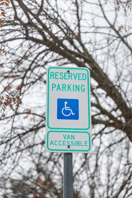 A reserved parking sign indicating designated space for disabled parking and van accessibility, mounted on a metal pole outdoors against a backdrop of bare tree branches and an overcast sky. The sign features a blue wheelchair symbol and green text stating 'RESERVED PARKING' and 'VAN ACCESSIBLE,' reflecting parking regulations relevant for home relocation and moving services. The image emphasizes compliance with parking permits required for the efficient loading and unloading of furniture and belongings during removals within the Knightsbridge area, as managed by Man with Van Knightsbridge.